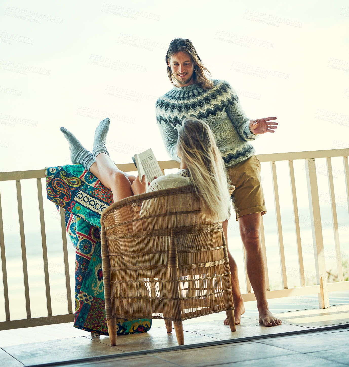 Buy stock photo Shot of a young man chatting with his girlfriend while she reads a book out on the balcony