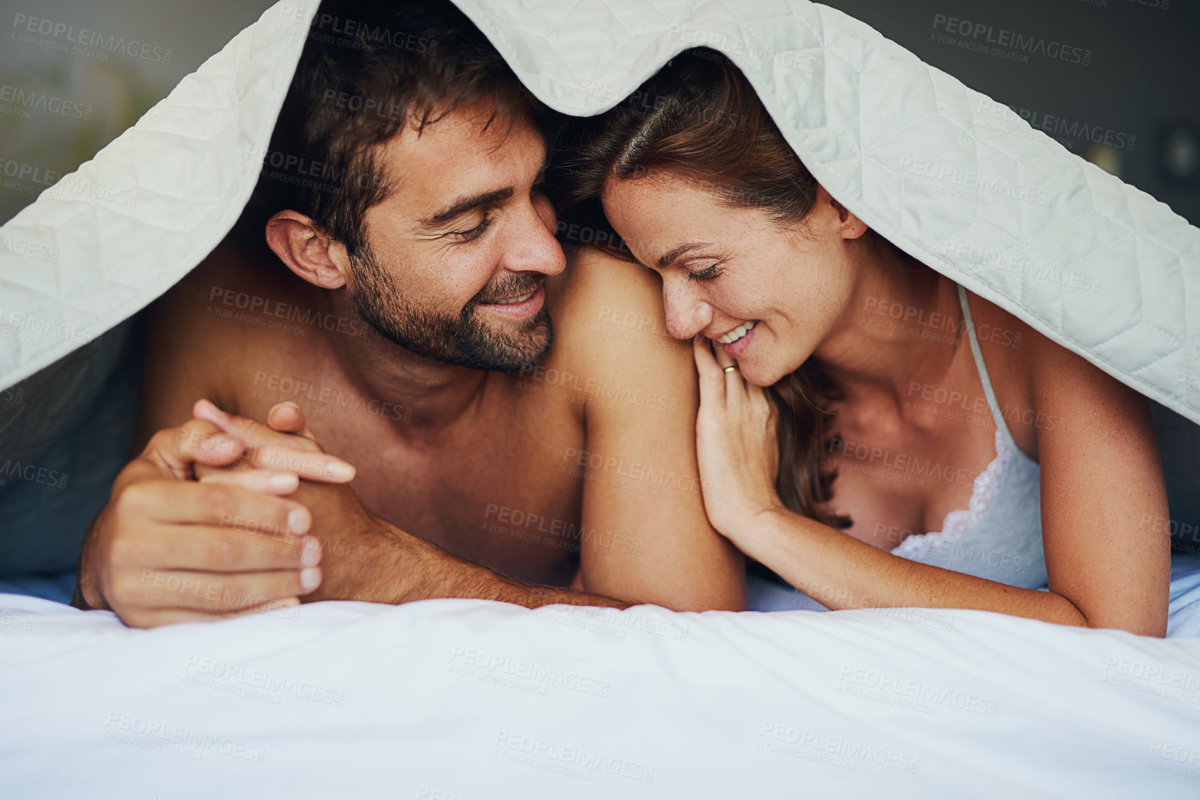 Buy stock photo Happy couple, relax and bed with sheets for love, bonding or awake from morning together at home. Man and woman lying with smile under duvet, fabric or linen in bedroom for care, support or affection