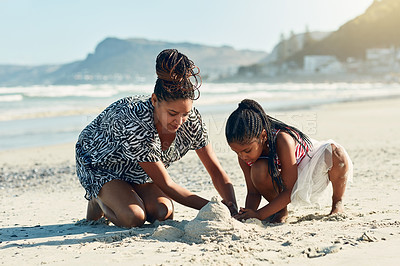 Buy stock photo Shot of a mother and her little daughter building a sandcastle together at the beach