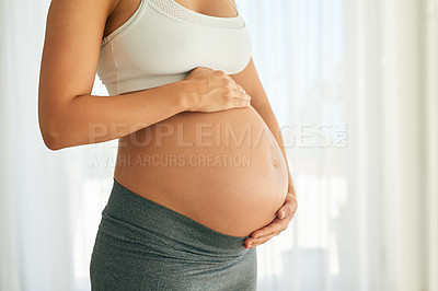 Buy stock photo Cropped shot of a pregnant woman holding her belly while sitting on her bed