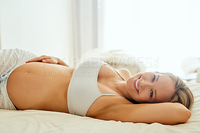 Buy stock photo Shot of a pregnant woman touching her belly while lying on her bed