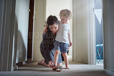 Buy stock photo Shot of a mother helping her son put his shoes on at home