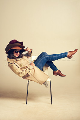 Buy stock photo Studio shot of a young woman sitting on a chair and wearing a pile of hats against a brown background