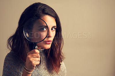 Buy stock photo Studio portrait of a young woman looking through a magnifying glass against a brown background