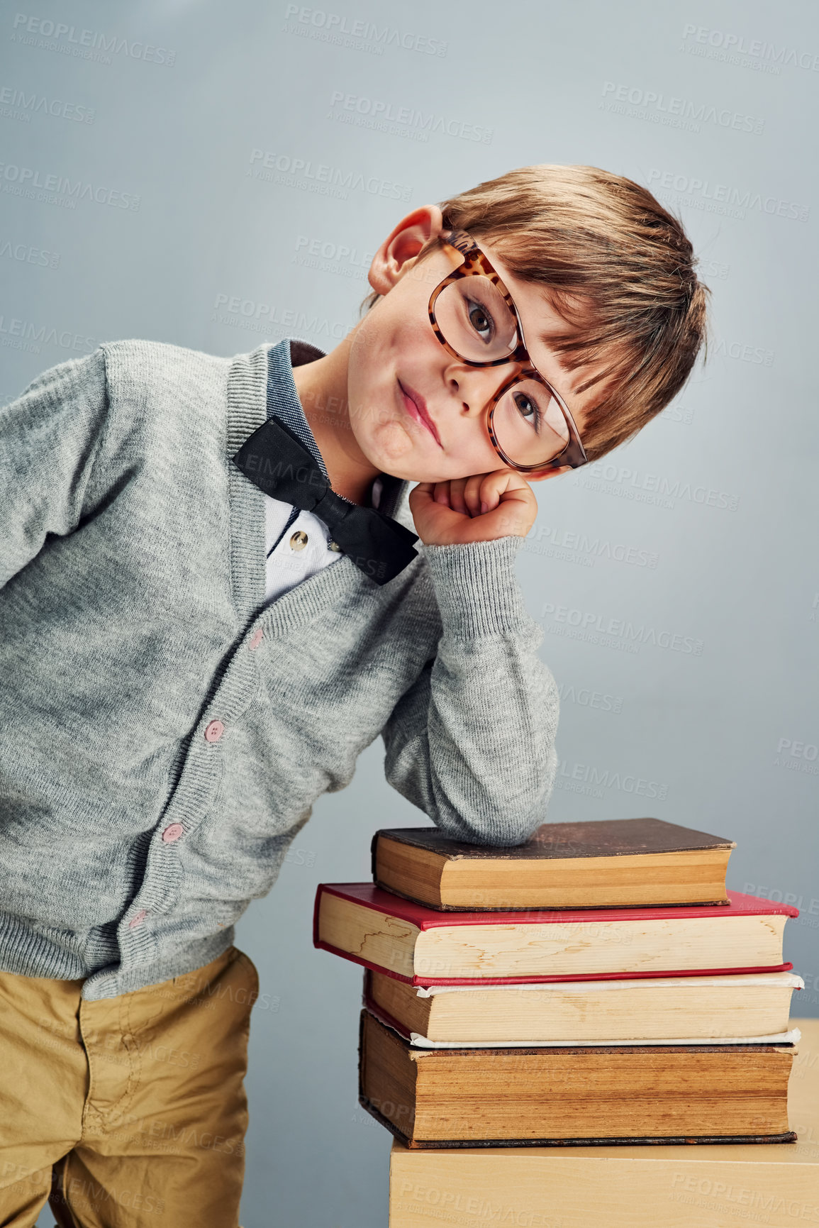 Buy stock photo Studio portrait of a smart little boy leaning over a pile of books against a gray background