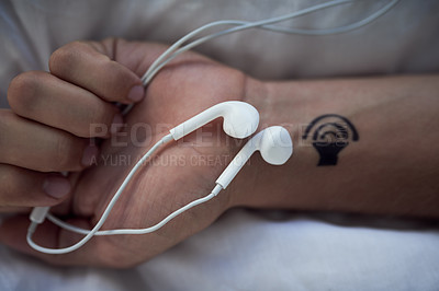 Buy stock photo Cropped shot of earphones in an unrecognizable person's closed hands and a tattoo of a speaker on his wrist