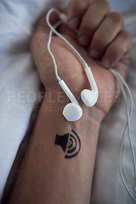 Buy stock photo Cropped shot of earphones in an unrecognizable persons's closed hands and a tattoo of a speaker on his wrist