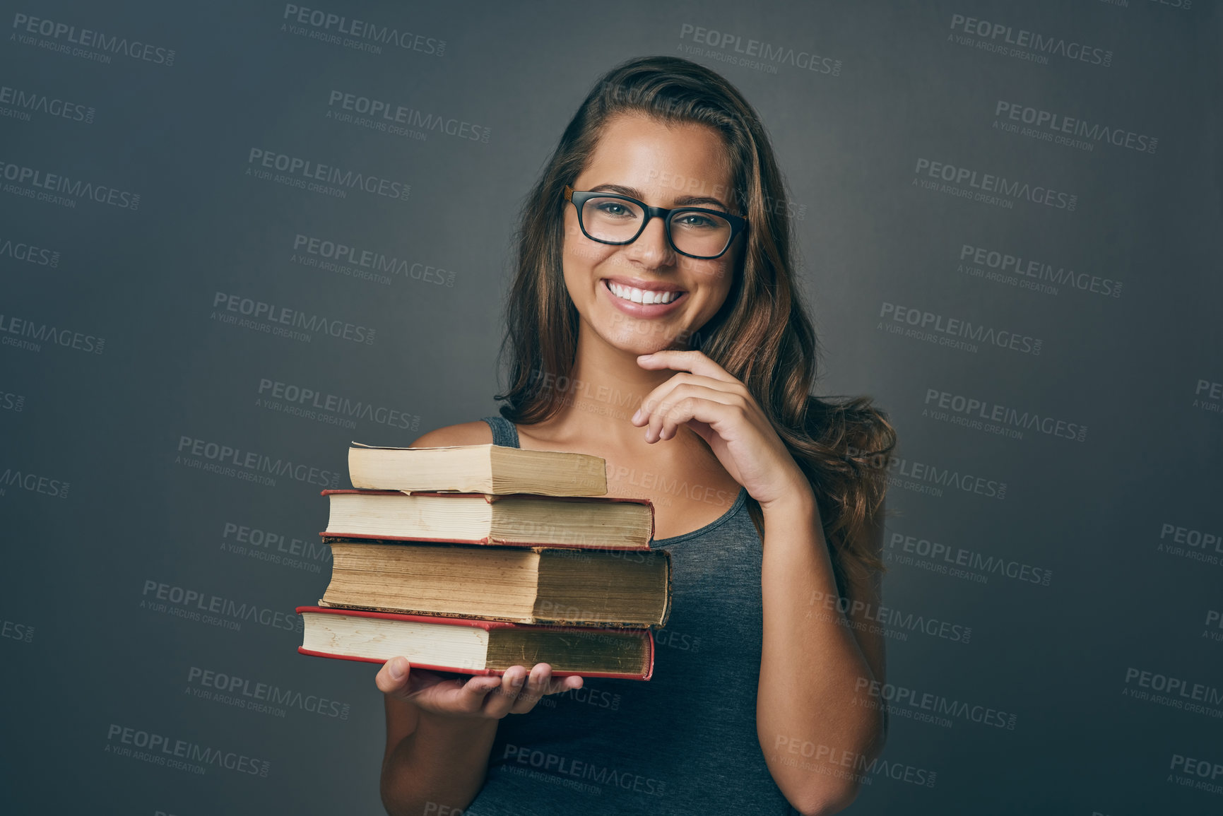 Buy stock photo Studio shot of a young woman holding a pile of books against a grey background