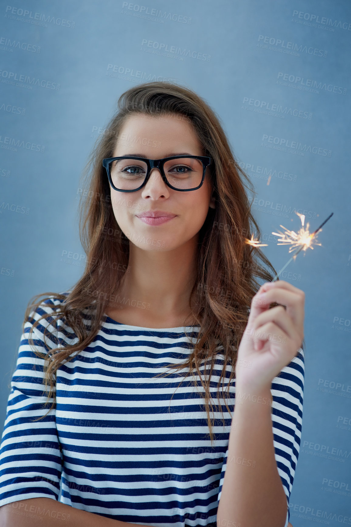 Buy stock photo Woman, hand and sparkler in studio with glasses for celebration isolated on blue background with glow. Smile, person and fun happy event with birthday or new year with light, portrait and fireworks.