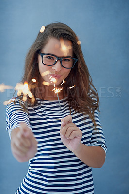 Buy stock photo Woman, smile and portrait in studio with sparklers for celebration isolated on blue background with light. Confidence, glasses and fun event with birthday or new year with glow, vision and fireworks.