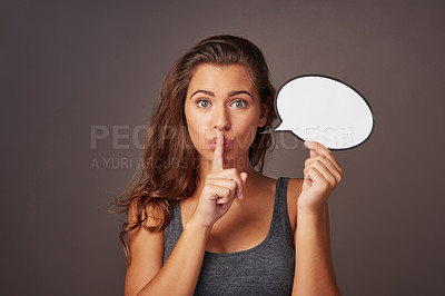 Buy stock photo Studio shot of an attractive young woman holding a blank speech bubble and whispering against a gray background