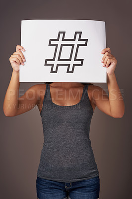 Buy stock photo Studio shot of a young woman holding a sign with a hashtag printed on it against a gray background