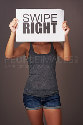 Buy stock photo Studio shot of a young woman holding a sign with swipe right printed on it against a gray background