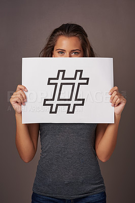 Buy stock photo Studio shot of a young woman holding a sign with a hashtag printed on it against a gray background