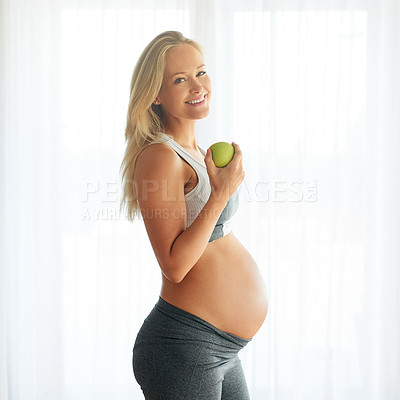 Buy stock photo Portrait of a happy pregnant woman dressed in sportswear and eating an apple at home