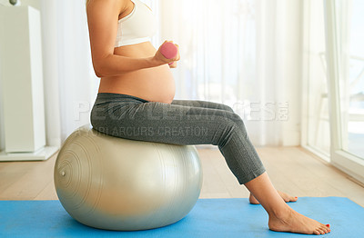 Buy stock photo Cropped shot of a pregnant woman working out with an exercise ball and weights at home