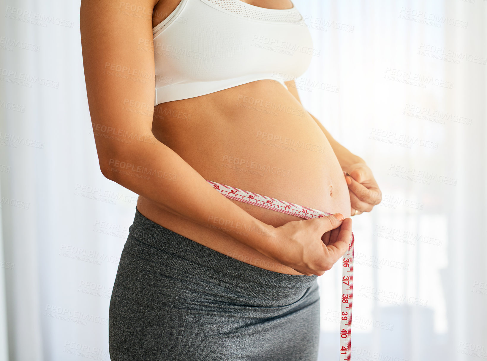 Buy stock photo Cropped shot of a pregnant woman measuring her belly at home