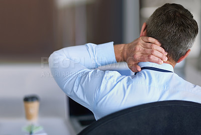 Buy stock photo Rearview shot of an unidentifiable businessman rubbing his sore neck while sitting in an office chair