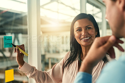 Buy stock photo Shot of a confident businesswoman presenting an idea to her colleague using adhesive notes on a glass wall in the office