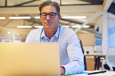 Buy stock photo Shot of a hardworking businessman using his laptop at his desk in the office