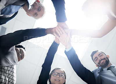 Buy stock photo Low angle portrait of a team of happy colleagues putting their hands on top of each other in the office