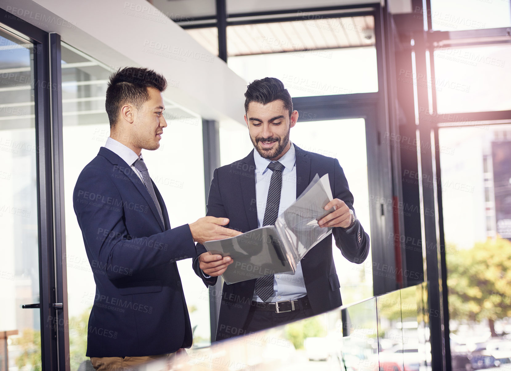 Buy stock photo Shot of two happy business partners discussing paperwork in the hallway in their office