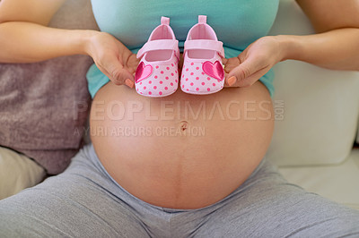 Buy stock photo Closeup shot of a pregnant woman holding a pair of pink baby shoes against her belly at home