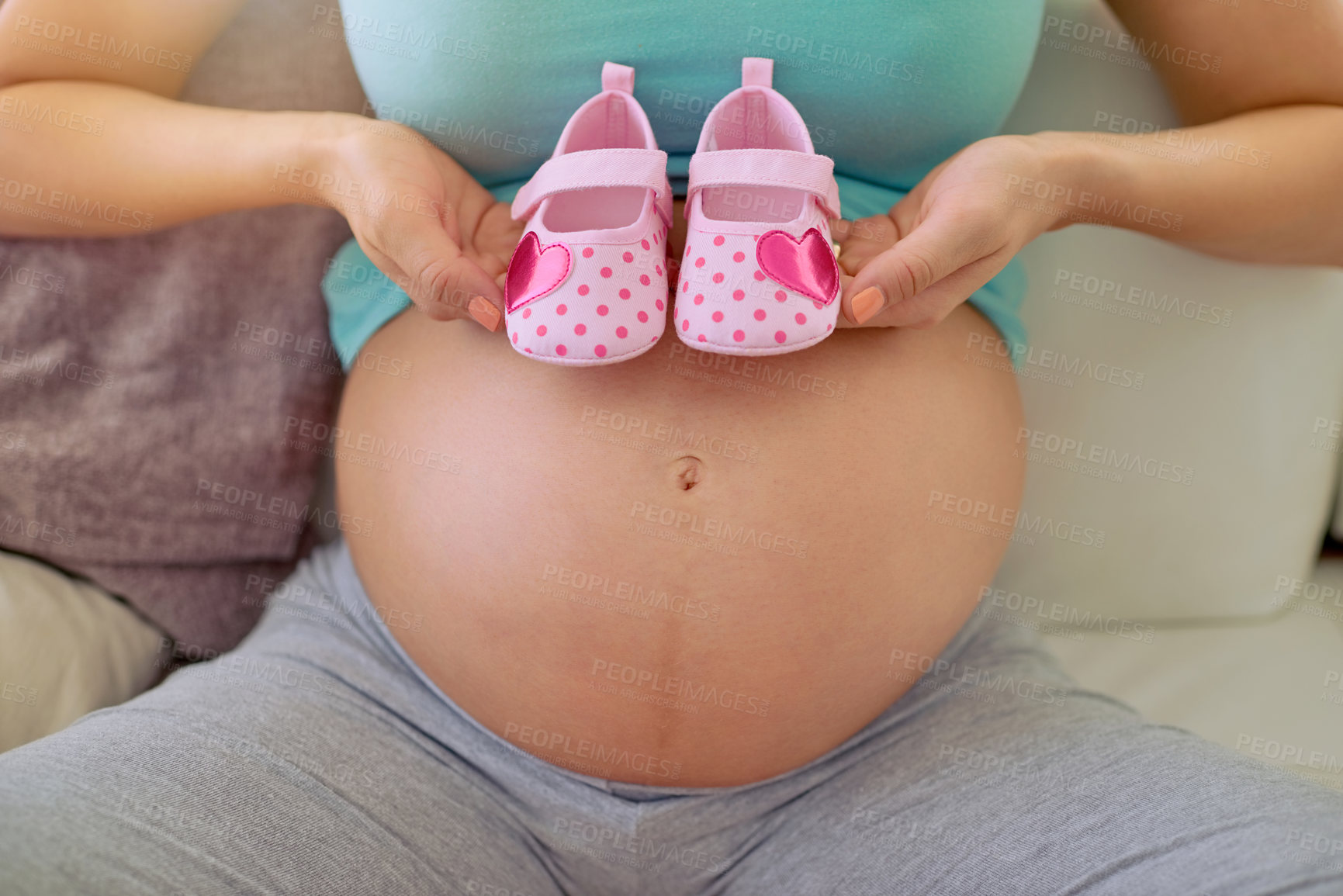 Buy stock photo Closeup shot of a pregnant woman holding a pair of pink baby shoes against her belly at home