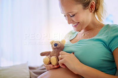 Buy stock photo Shot of a pregnant woman holding a teddy bear while relaxing at home