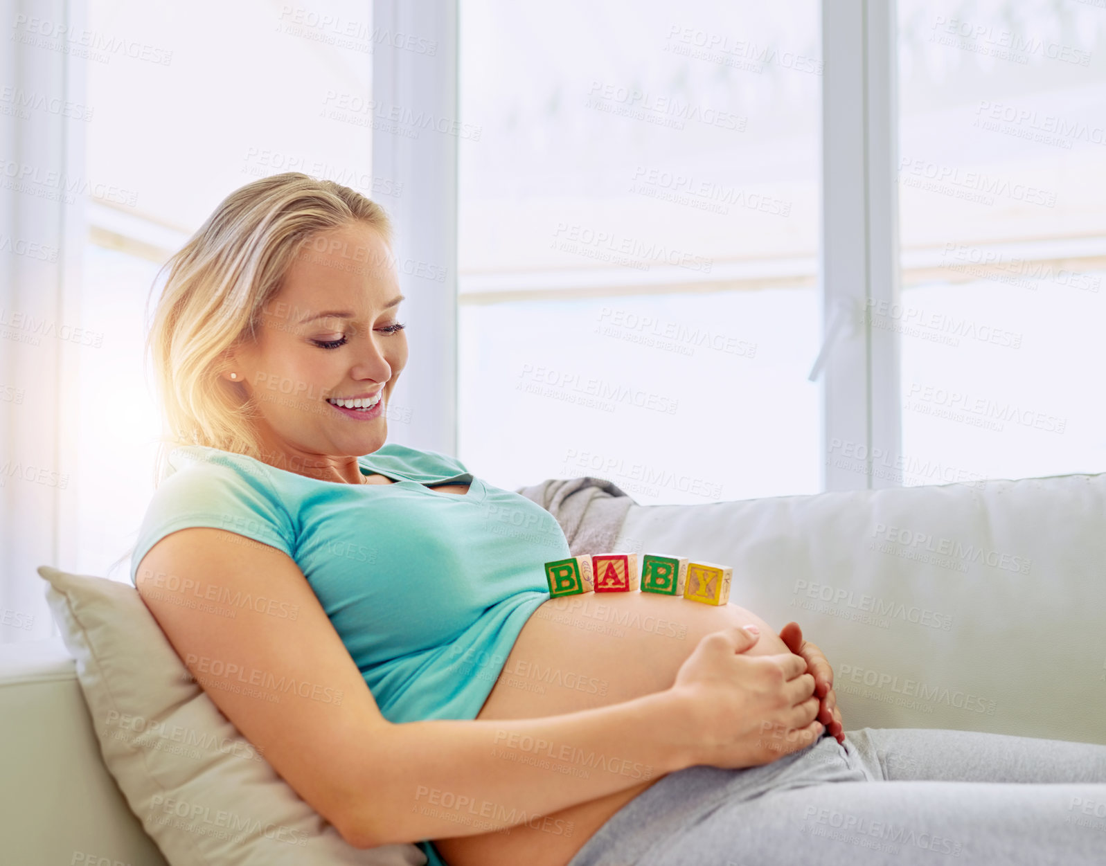 Buy stock photo Shot of a pregnant woman lying down with wooden baby blocks on her belly at home