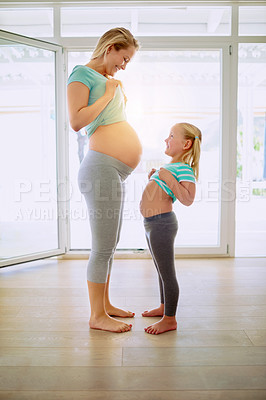 Buy stock photo Shot of a pregnant woman and her little daughter showing each other their stomachs at home