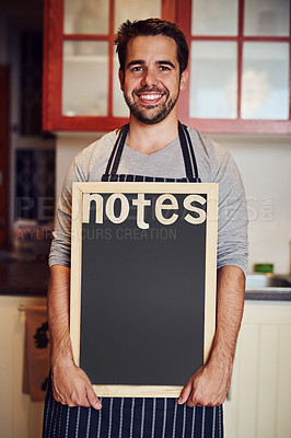 Buy stock photo Portrait of a happy young man holding a blank chalkboard while standing in his kitchen at home
