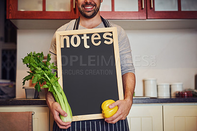 Buy stock photo Cropped shot of an unidentifiable young man holding a blank chalkboard while standing in his kitchen at home