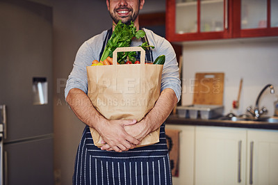 Buy stock photo Cropped shot of an unidentifiable young man holding a bag of groceries in his kitchen at home