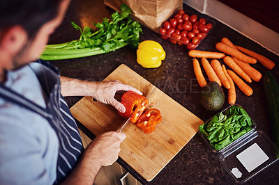 Buy stock photo High angle shot of an unidentifiable young man chopping vegetables in his kitchen at home