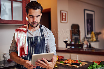 Buy stock photo Shot of a happy young man using his tablet while cooking in his kitchen at home