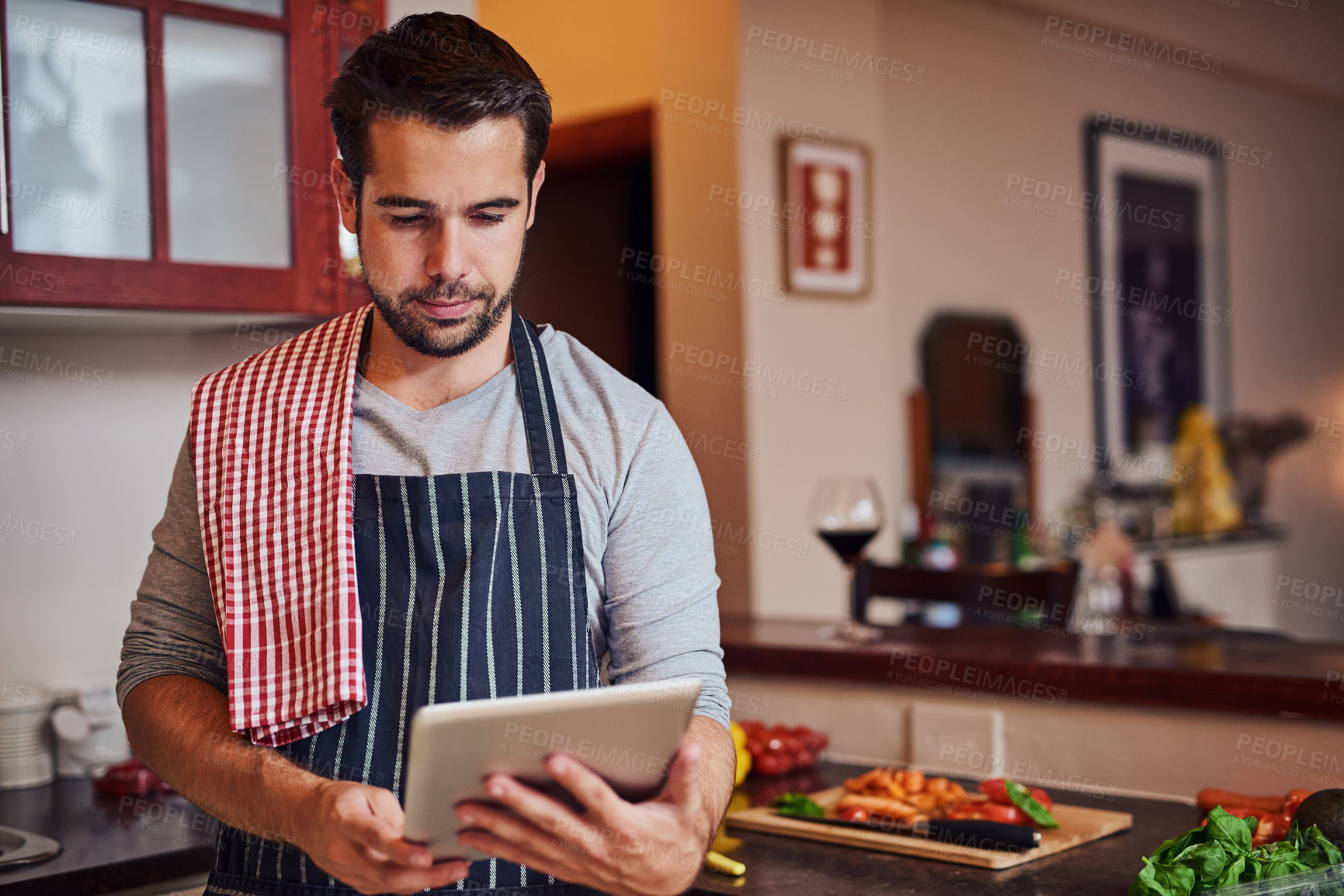 Buy stock photo Shot of a happy young man using his tablet while cooking in his kitchen at home