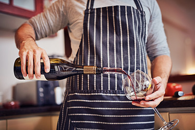Buy stock photo Cropped shot of an unidentifiable young man pouring a glass of wine while cooking in his kitchen at home
