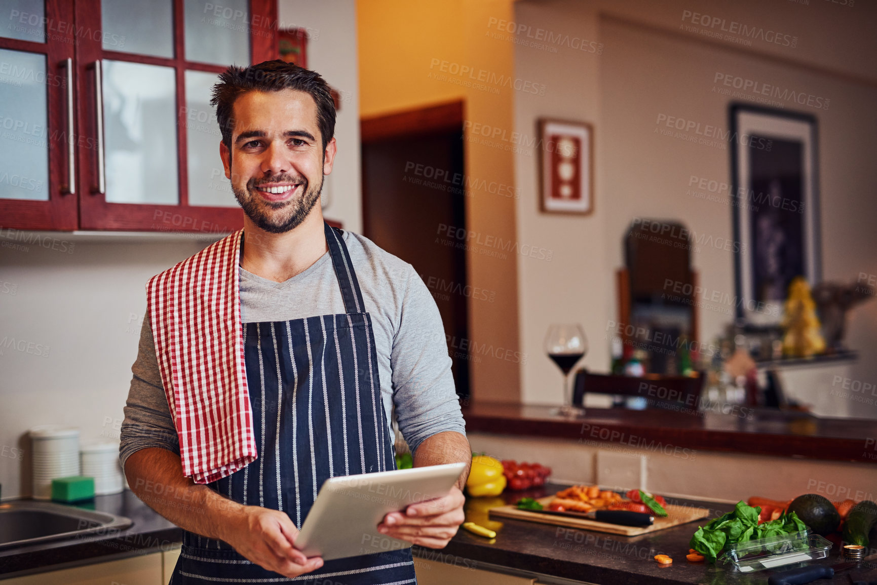 Buy stock photo Portrait of a happy young man using his tablet while cooking in his kitchen at home