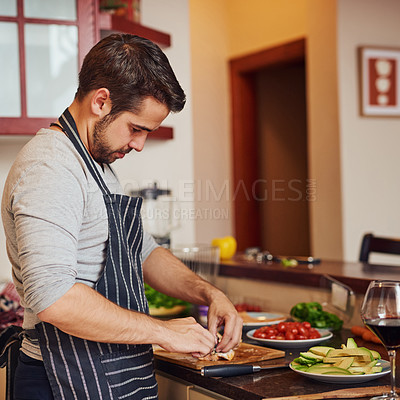 Buy stock photo Shot of a happy young man chopping vegetables in his kitchen at home