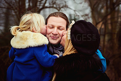 Buy stock photo Shot of a mother and daughter kissing the father on the cheeks outdoors