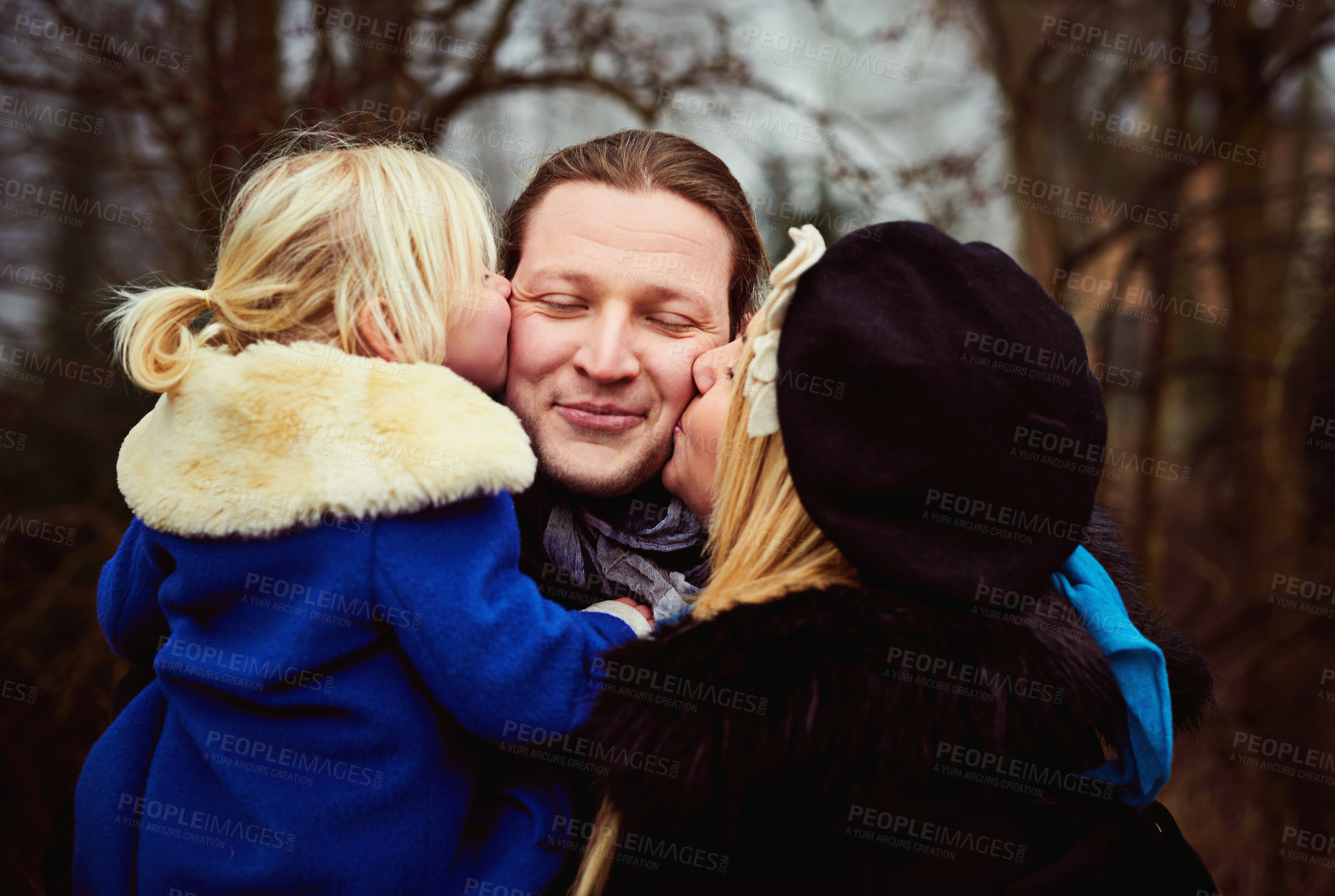 Buy stock photo Shot of a mother and daughter kissing the father on the cheeks outdoors