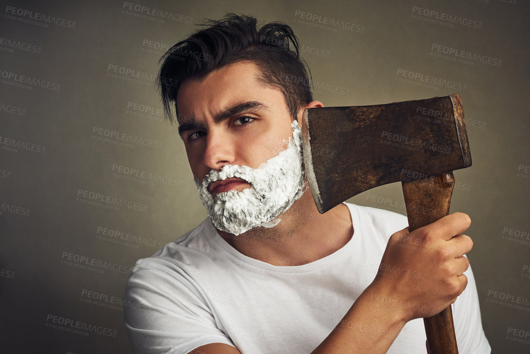 Buy stock photo Shot of a handsome young man shaving his beard with a lumberjack