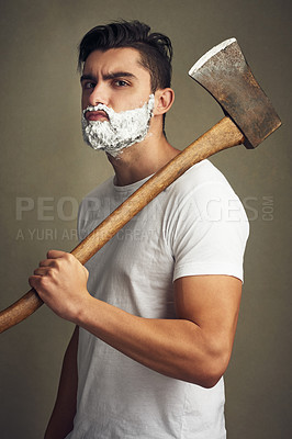 Buy stock photo Shot of a handsome young man shaving his beard with a lumberjack