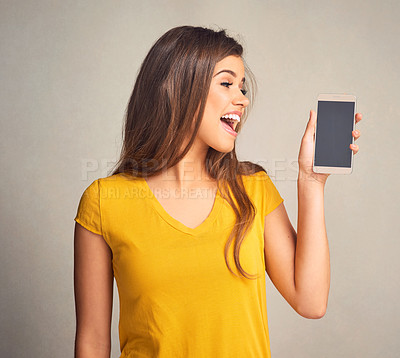 Buy stock photo Shot of an attractive young woman holding a cellphone with a blank screen against a grey background