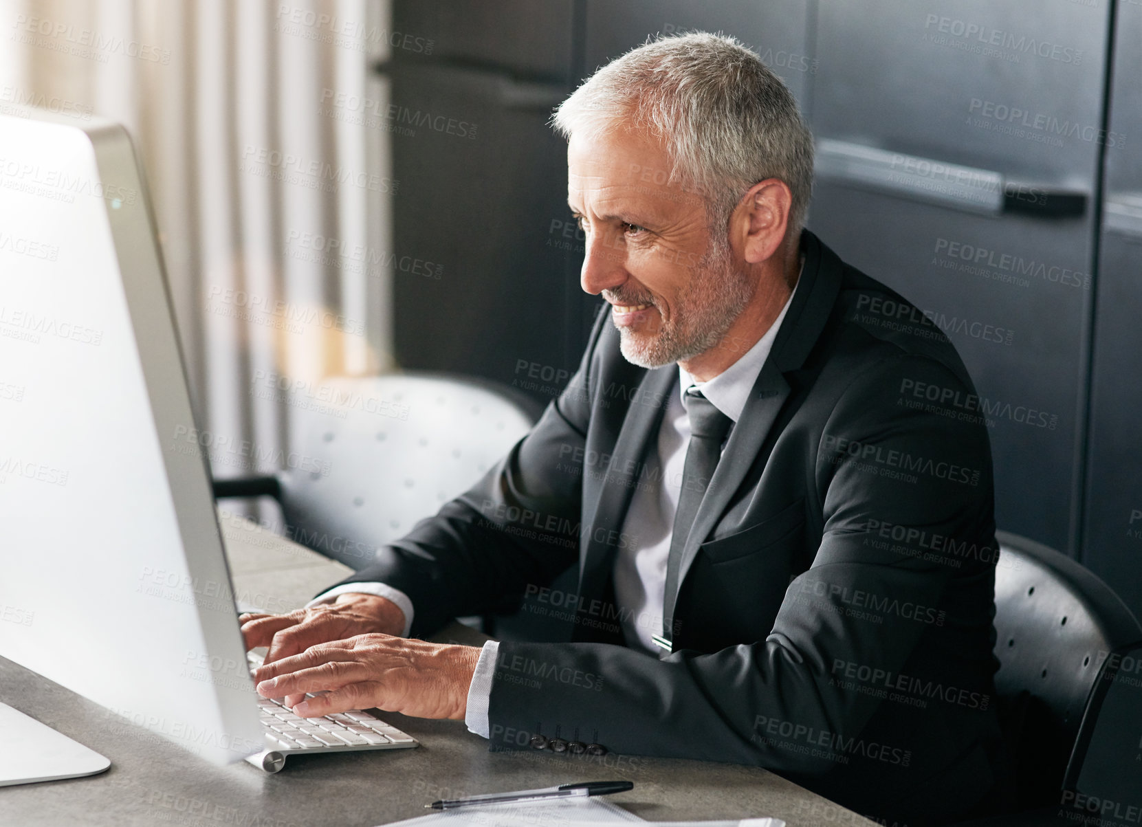 Buy stock photo Cropped shot of a handsome mature businessman sitting down and working on his computer in the office