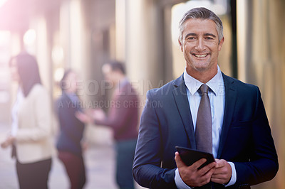 Buy stock photo Shot of a mature businessman standing and looking confident while using his tablet outside in the streets