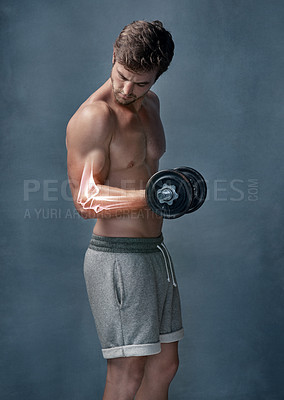 Buy stock photo Shot of a focussed young man experiencing elbow strain while working out with weights in the studio
