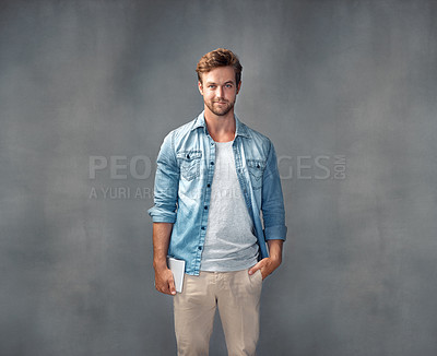 Buy stock photo Portrait of a handsome young man holding a tablet while posing against a gray background in the studio