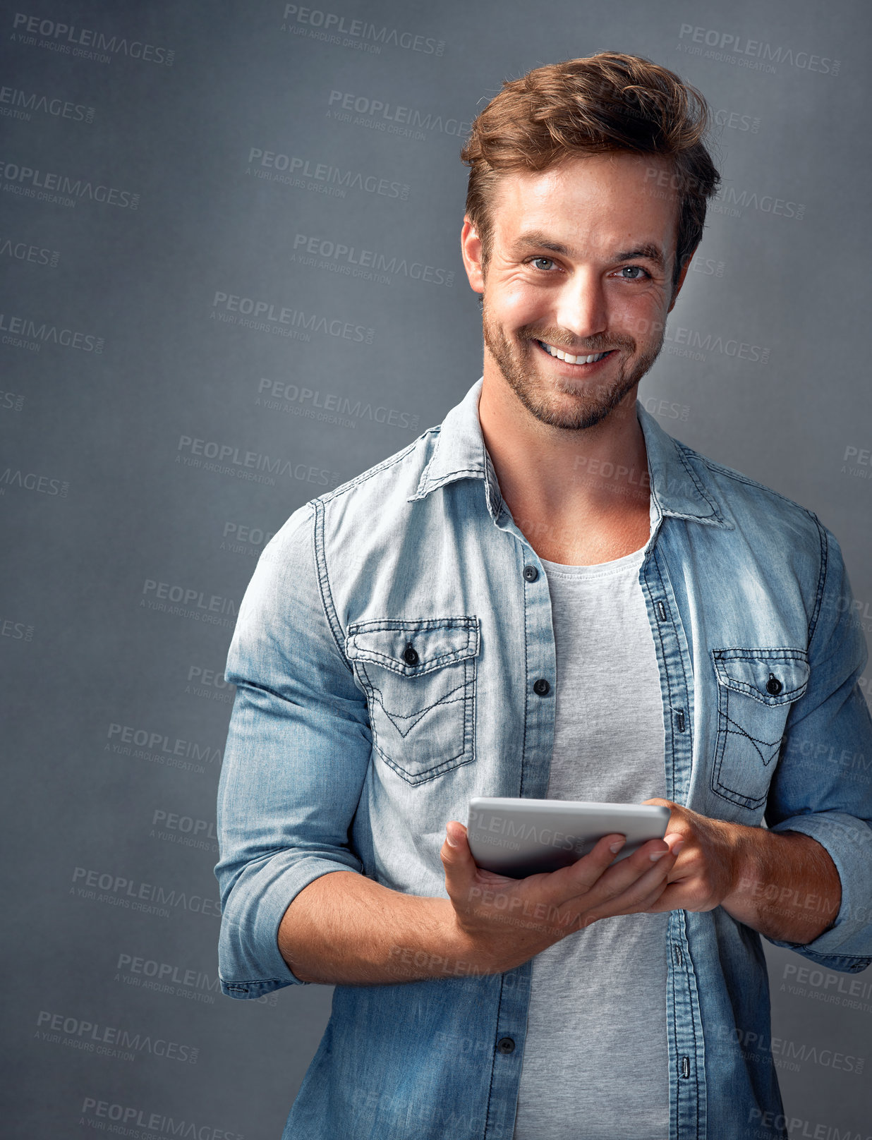 Buy stock photo Portrait of a handsome young man using a tablet against a gray background in the studio
